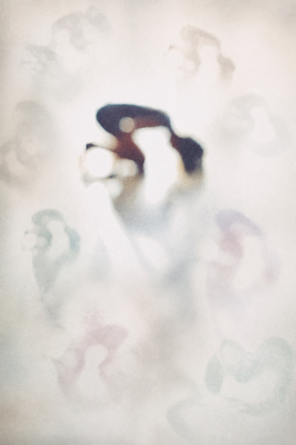 A softly focused curled human figure surrounded by faint exposure echoes and luminous negative space.